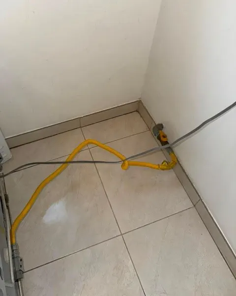 After: cleared tiled floor corner behind an appliance with a yellow hose and cable.
