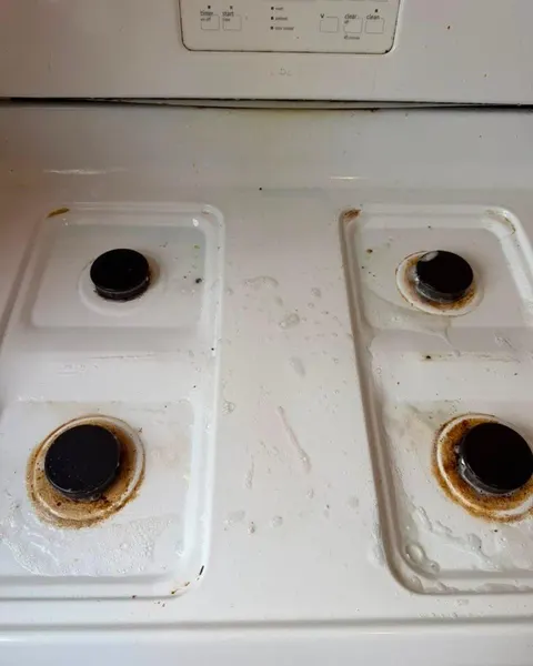 Before: white gas stovetop with brown residue around four burners.