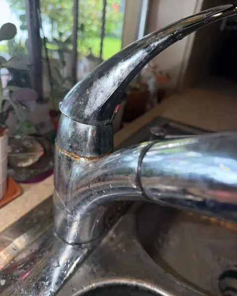 Before: chrome kitchen faucet with cloudy surface marks and residue around the handle joint.