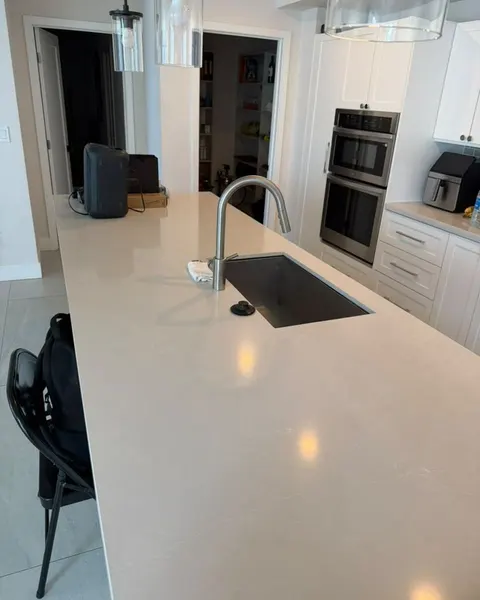 After: light kitchen island countertop with a sink and chrome faucet, white cabinets and built-in ovens.