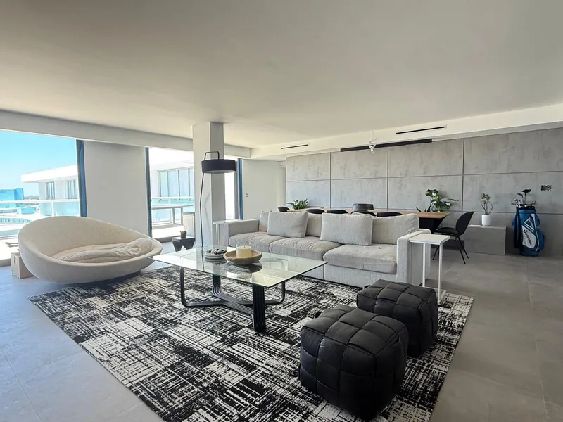 Sala con sofá color crema, sillón redondo, mesa de cristal y ventanales al balcón.