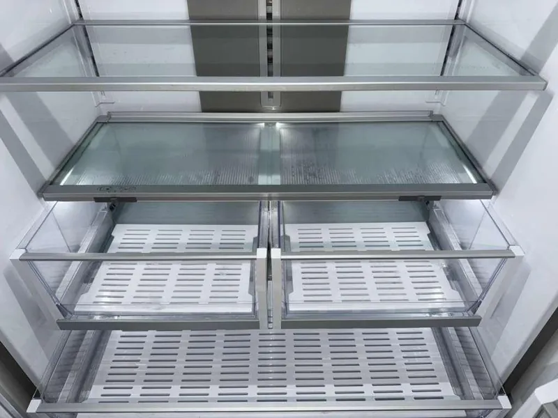Empty refrigerator interior with glass shelves and clear produce drawers.