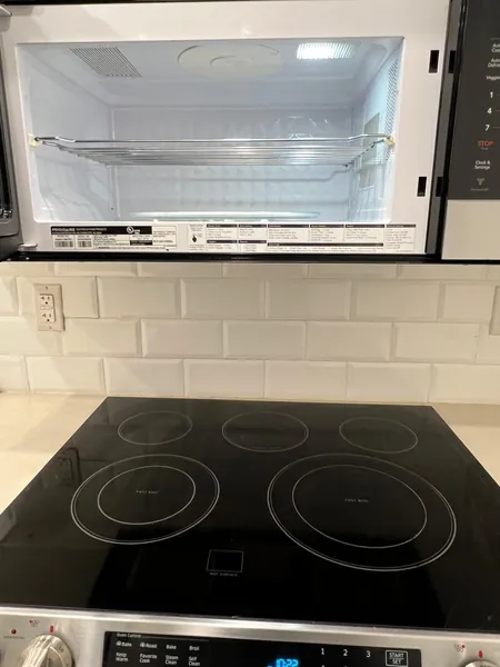Black glass stovetop beneath an open microwave with an empty interior.