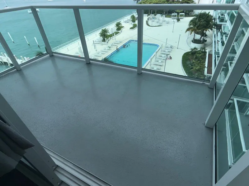 Empty balcony with a glass railing overlooking a pool and the water.